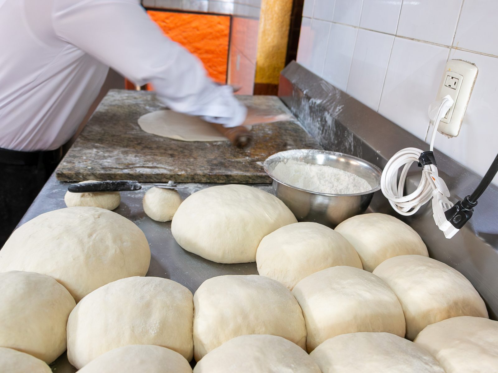 Manos del chef extendiendo la masa de pizza sobre una tabla de mármol, bolas de masa en primer plano